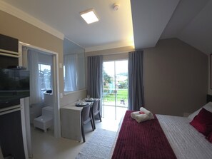 A hotel room with a bed, a desk, a television, and a view of the outdoors. - Pousada Retiro das Ilhas (Bombinhas)