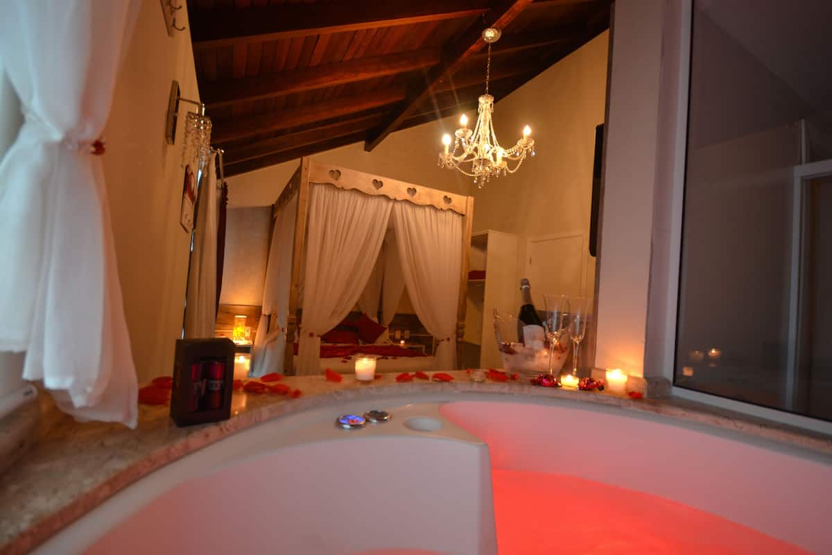 Ein luxuriöses Schlafzimmer mit einem großen Bett, einer Kristallleuchter und einer Badewanne mit Rosenblüten.