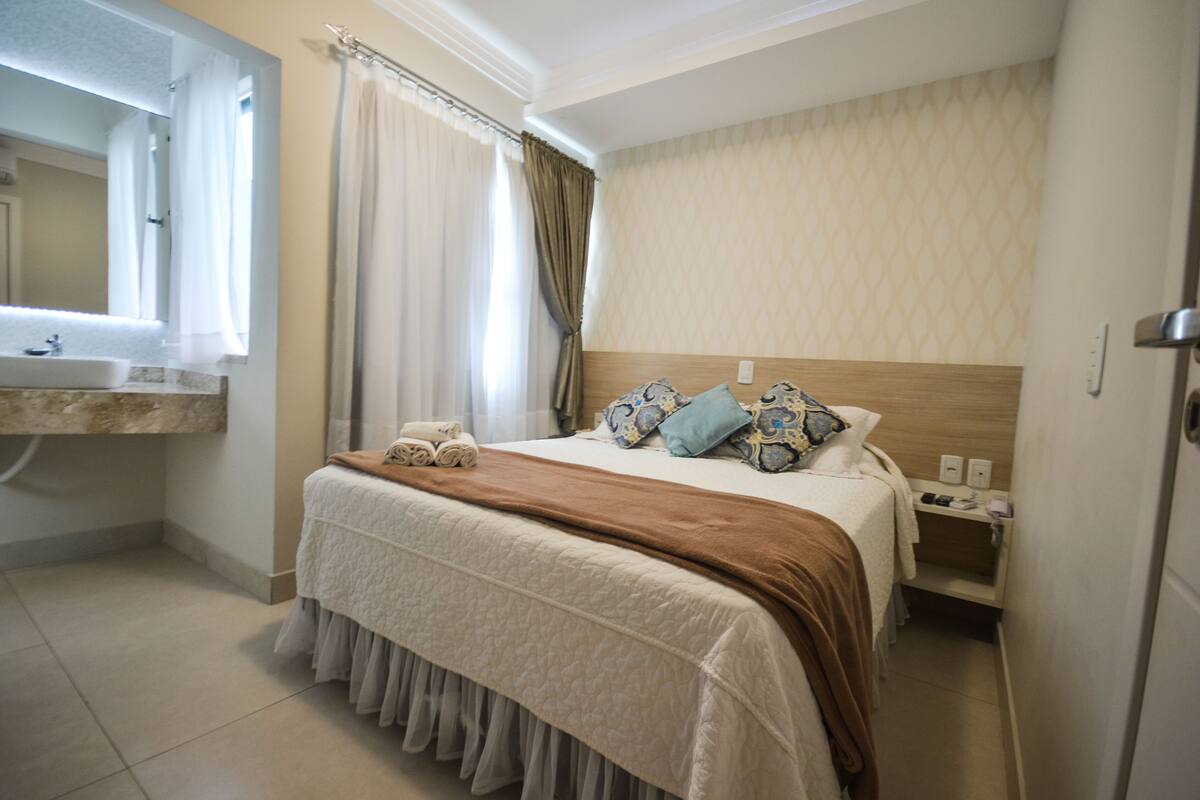 Ein Hotelzimmer mit Bett, Nachttisch, Badezimmer mit Waschbecken und Spiegel.