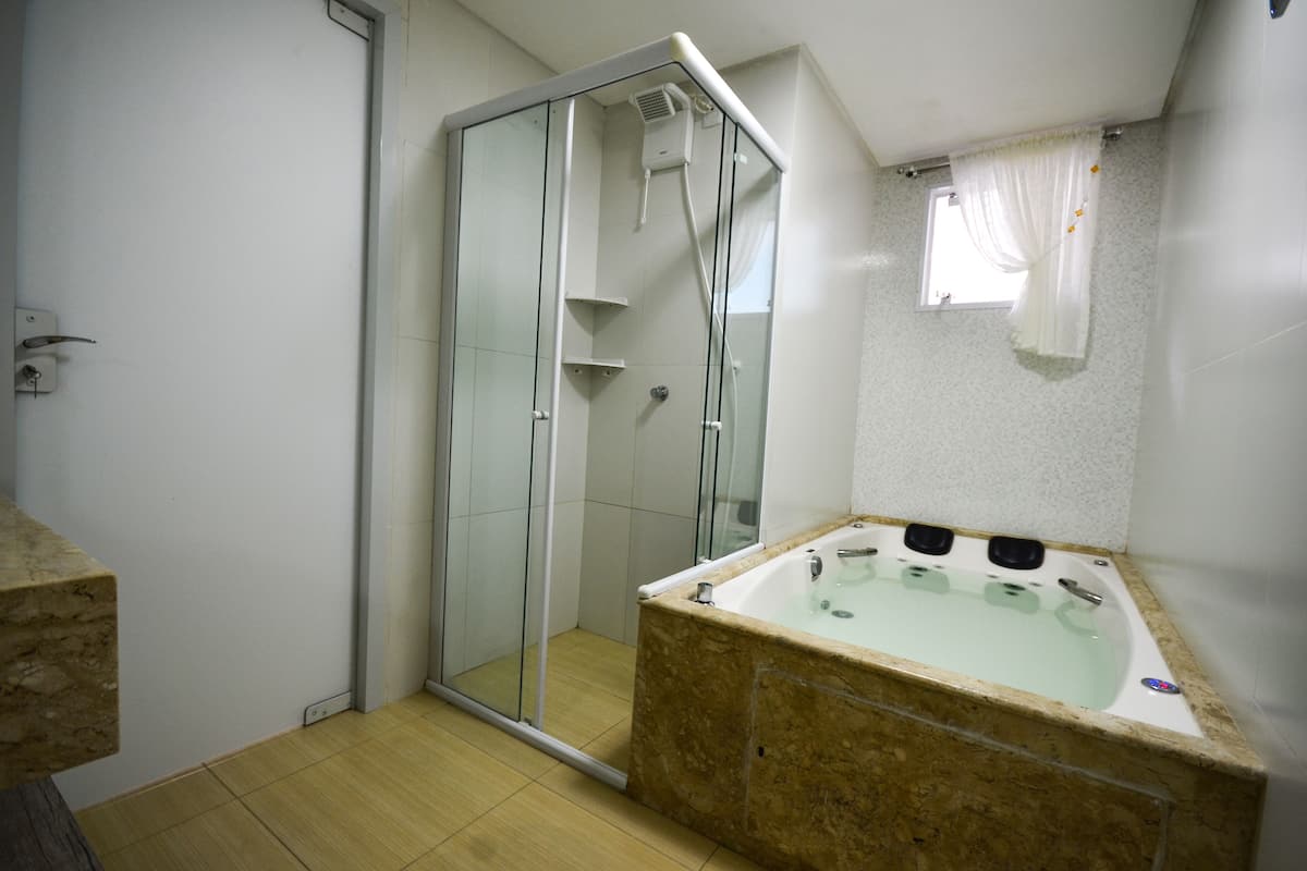 Ein Badezimmer mit einer gläsernen Duschkabine, einer Marmorbadewanne und einem kleinen Fenster mit Vorhang.