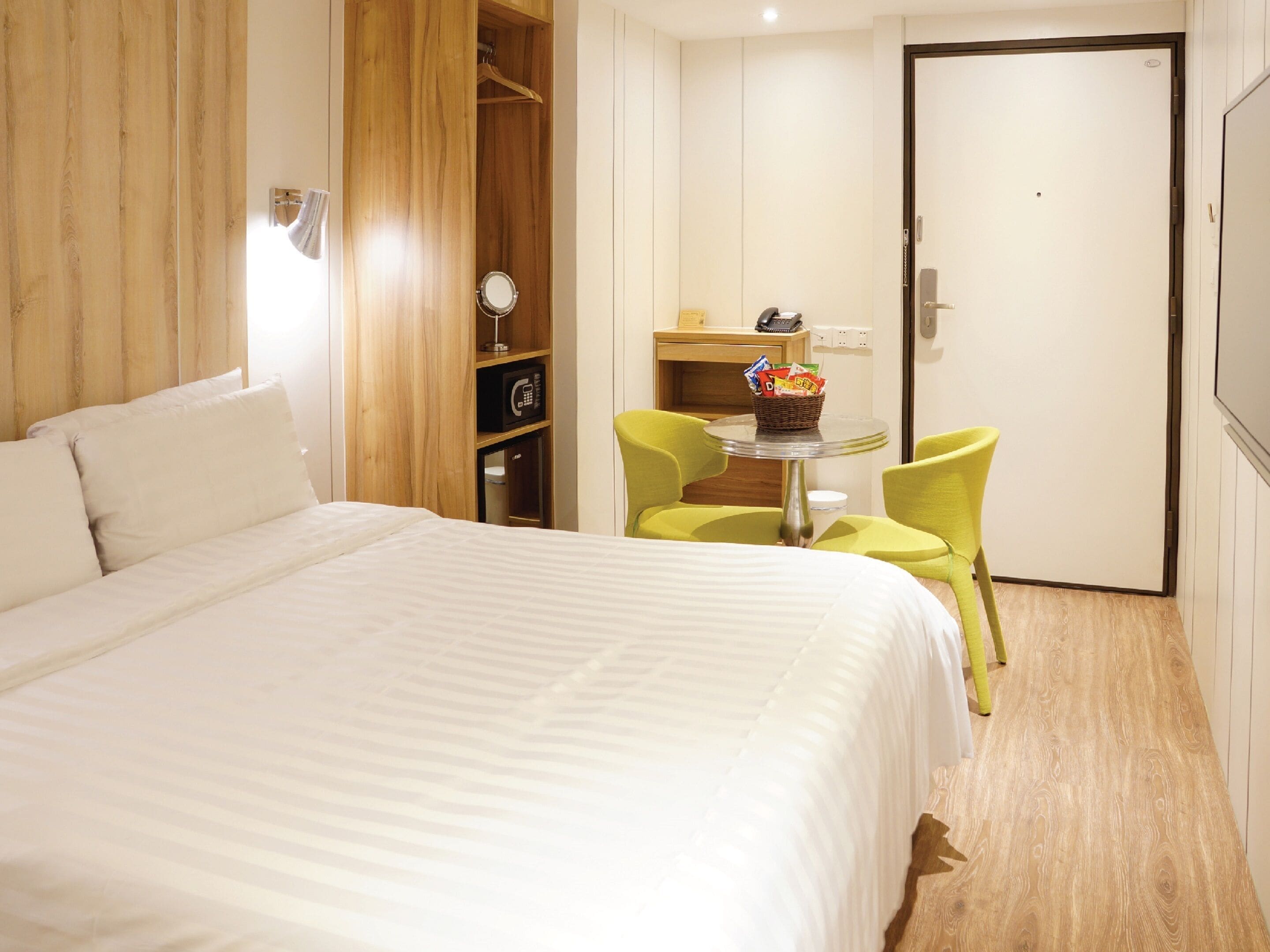 A hotel room with a large bed, a wooden wardrobe, a small table with chairs, and a door.