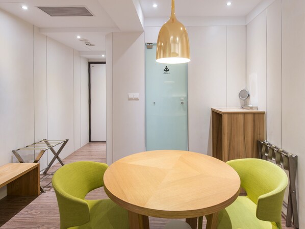 Een vergaderruimte met een ronde houten tafel, twee groene stoelen, een hangende kroonluchter en een houten kast met spiegel.