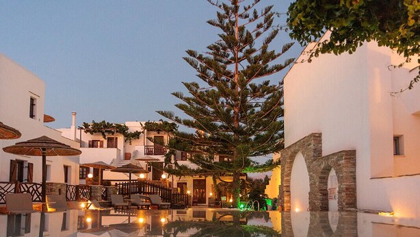 Un patio con un estanque reflectante, edificios blancos y un árbol grande.