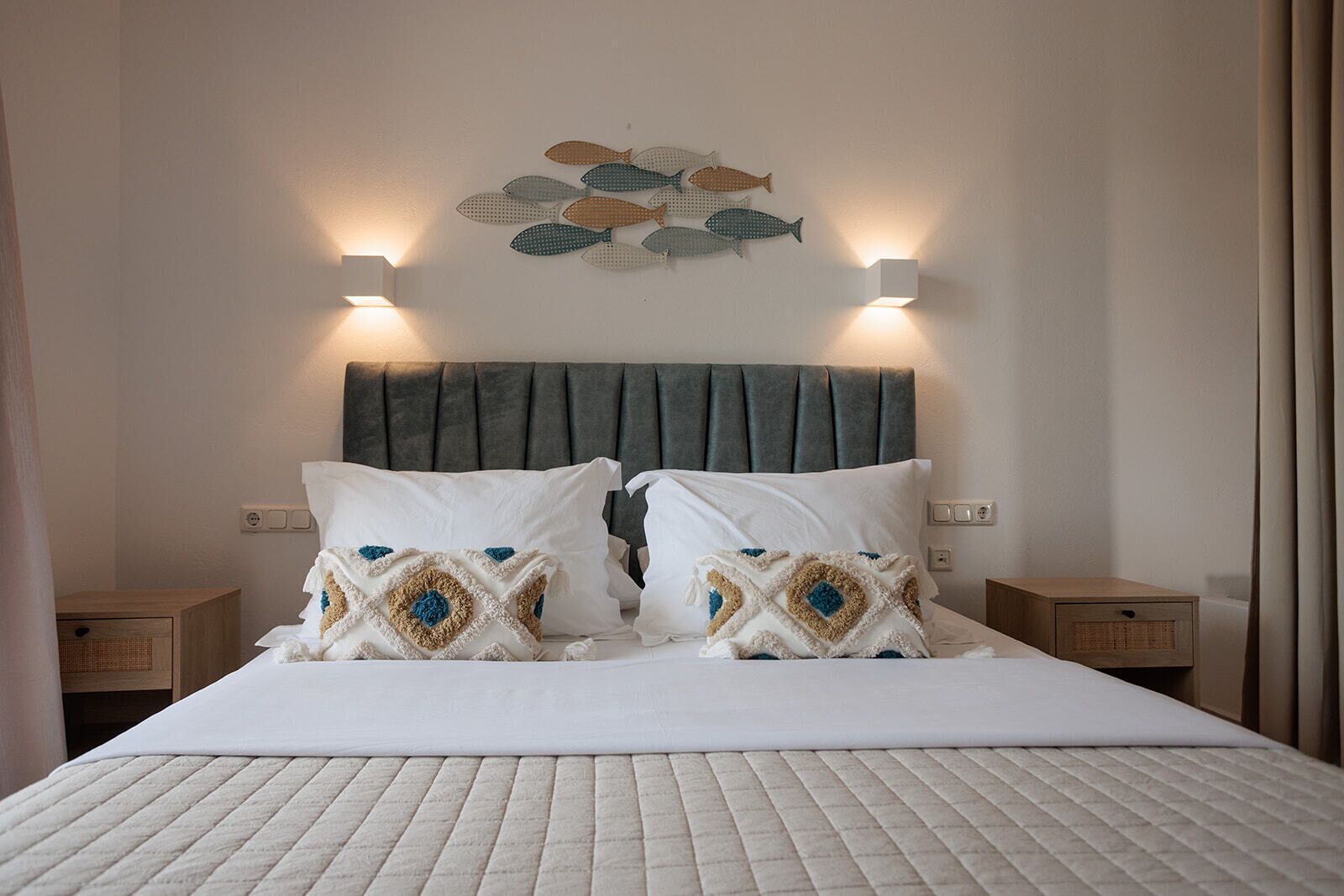 A neatly made bed with two decorative pillows, a headboard with built-in lighting, and a wall-mounted fish decoration.