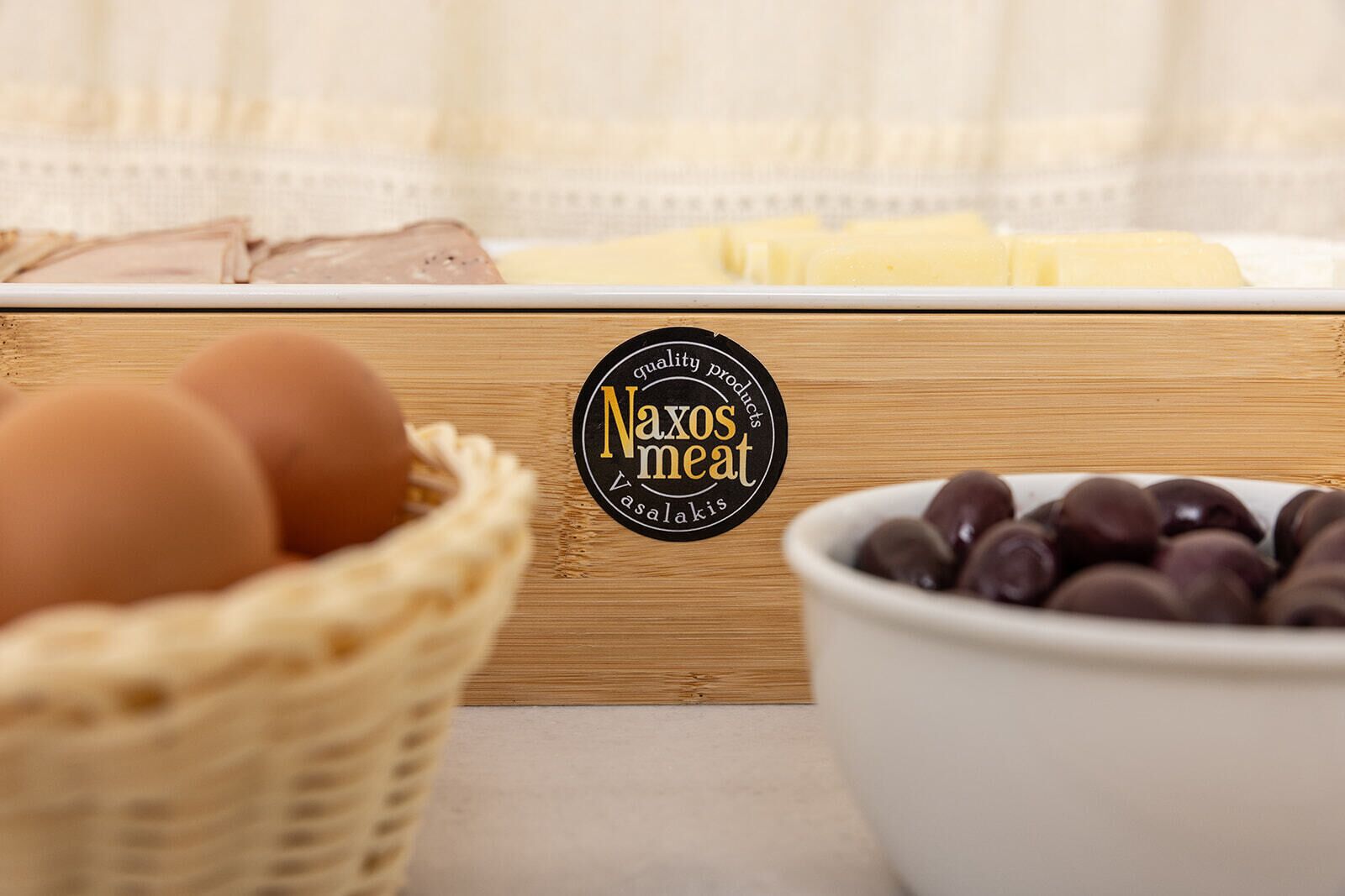 Laatikko Naxosin lihavalmisteita, jossa on logo, kori täynnä kananmunia ja kulho suklaakonvehteja.