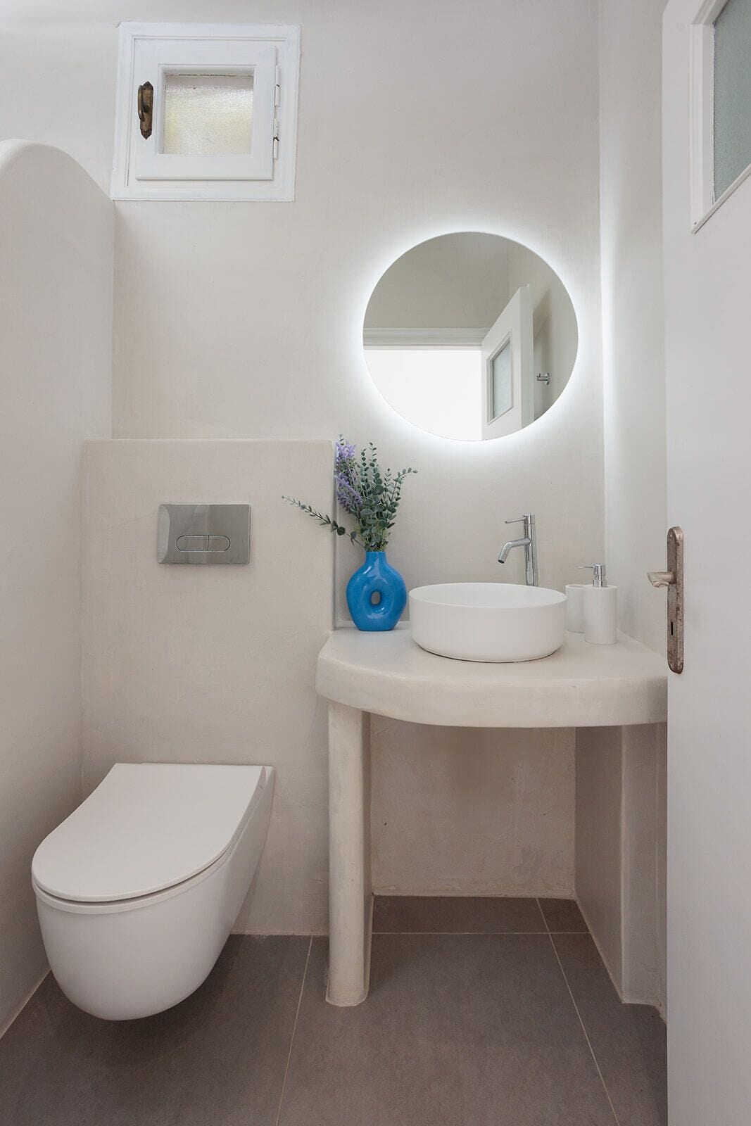A bathroom with a toilet, a sink with a mirror, and a wall-mounted light fixture.
