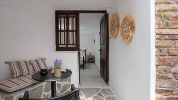 A cozy seating area with a sofa and a table, a wooden door leading to a hallway, and a stone wall with decorative wall art.