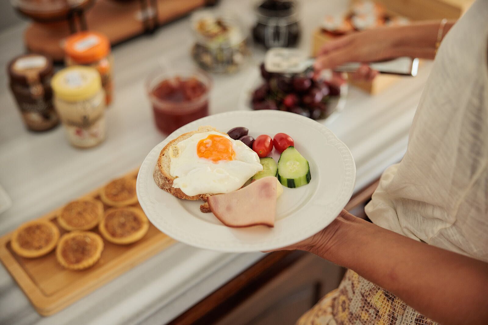Une personne tenant une assiette contenant des toasts, des œufs, du jambon et des légumes.