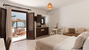 Una habitación de hotel con una cama, un escritorio, una silla, una mesita y vista al mar a través de una puerta abierta.