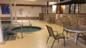 A pool area with a hot tub, a glass table, and chairs. There are stone walls and a wooden ceiling. - Landmark Motor Inn (Fort Edward)