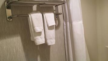 A bathroom with a towel rack holding folded towels and a shower curtain.