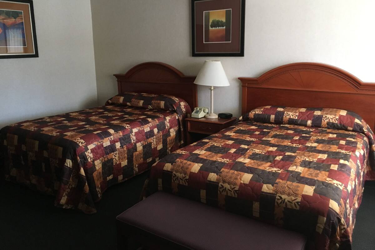 A hotel room with two single beds, a nightstand with a lamp, and a bench.