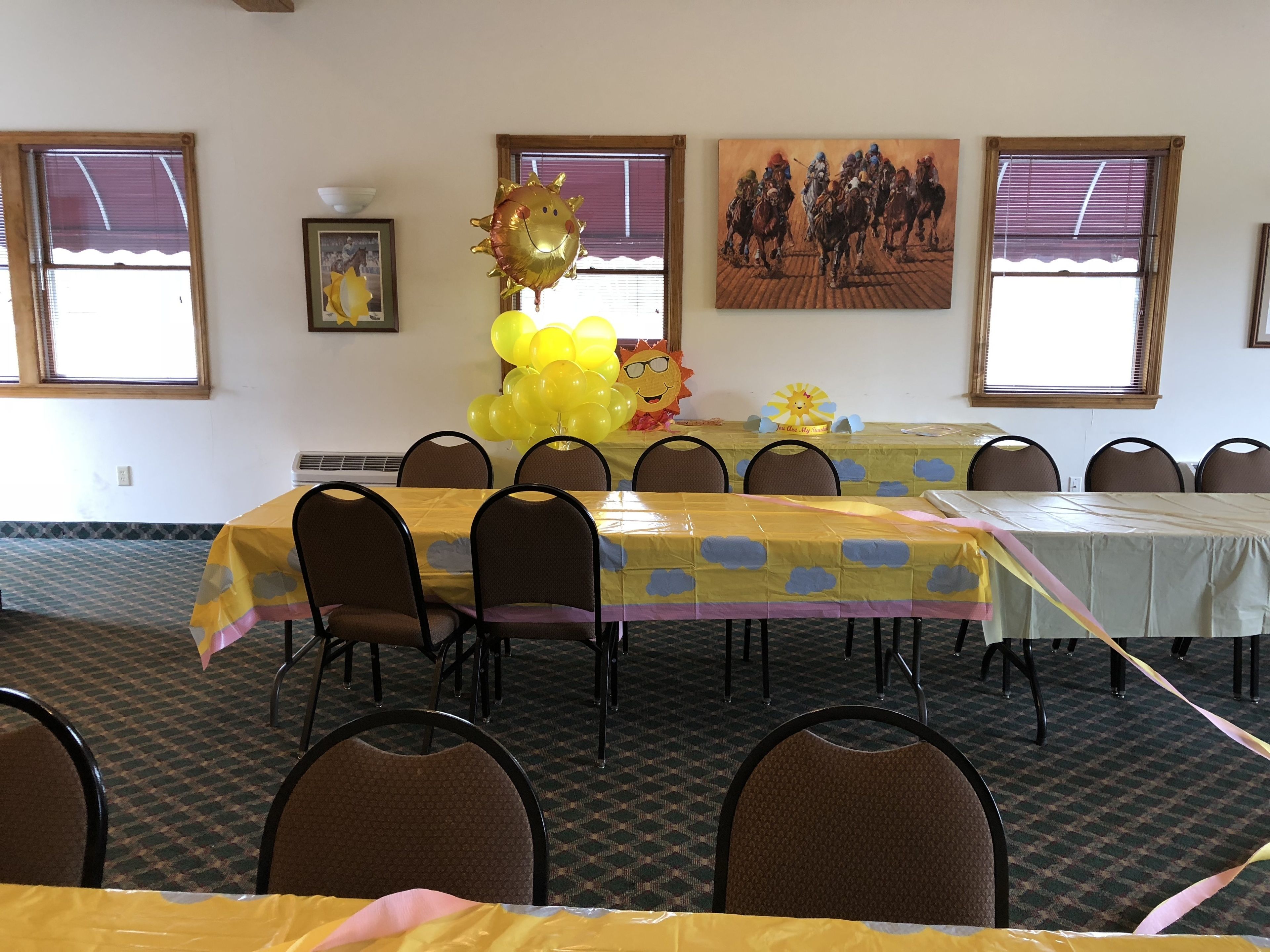 A conference room with tables covered in yellow tablecloths, chairs arranged around them, and balloons on the tables.