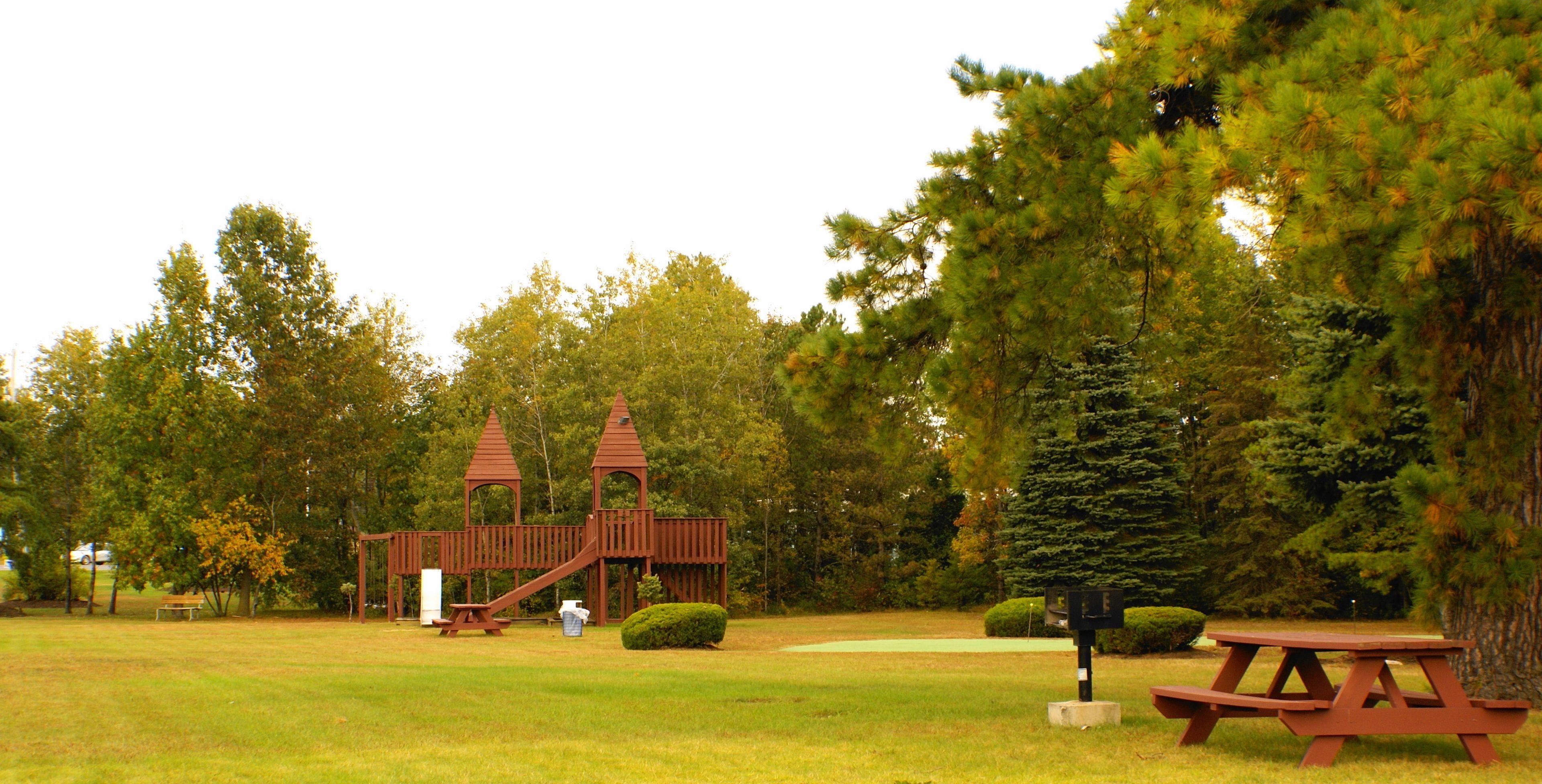 A playground with a wooden structure, picnic tables, and a well-maintained grassy area.