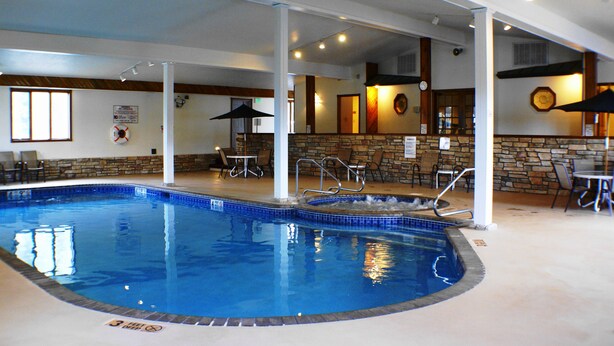 An indoor swimming pool with a stone wall, lounge chairs, and a bar area. - Landmark Motor Inn (Fort Edward)