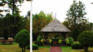 A gazebo with a tiled roof, surrounded by well-maintained grass and bushes, with a paved path leading to it. - Landmark Motor Inn (Fort Edward)