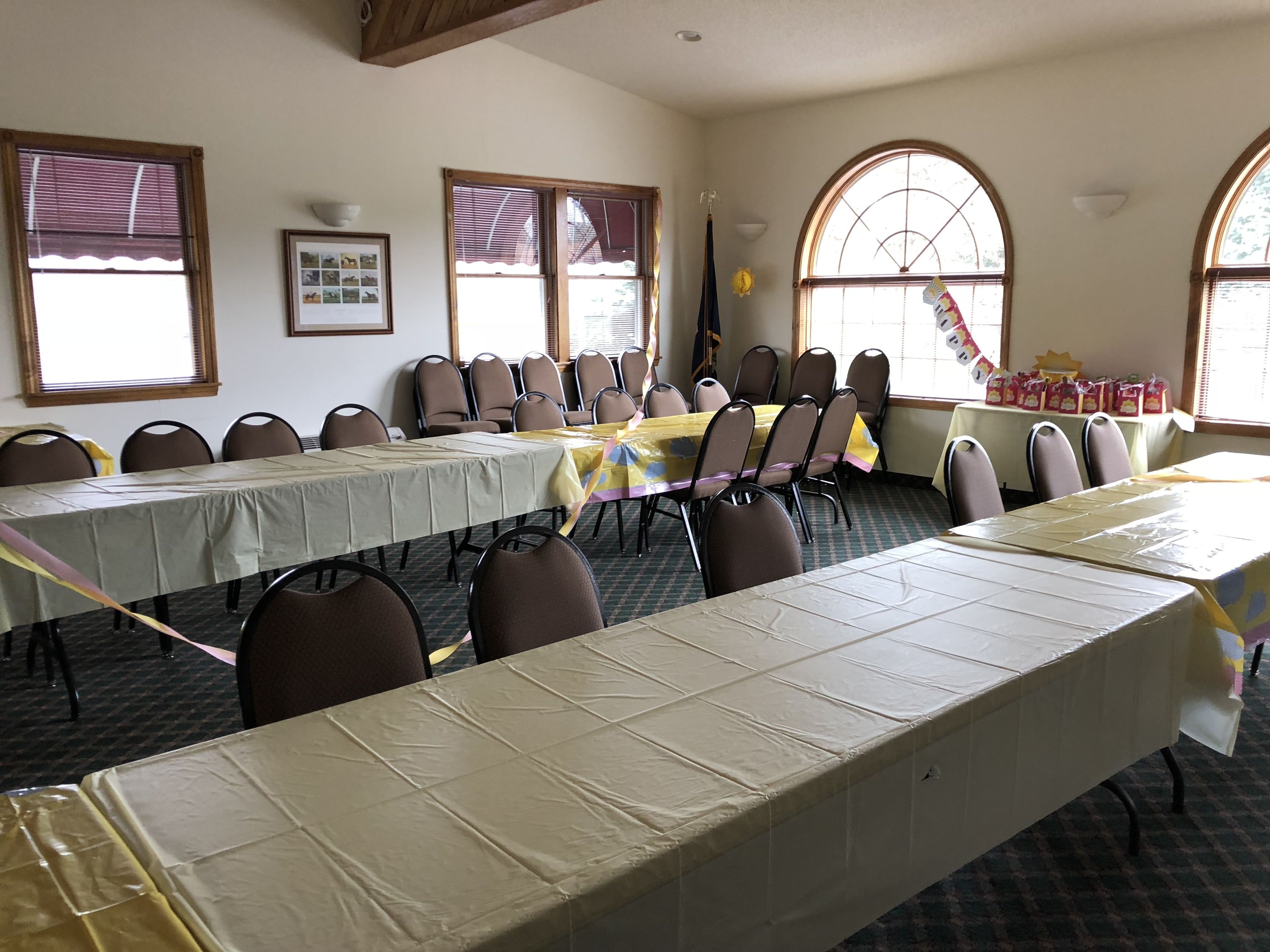 A conference room with long tables and chairs, large windows, and a framed picture on the wall.