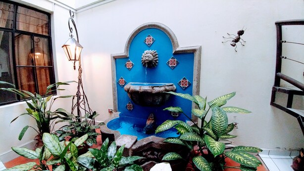 Un patio con una fuente azul, plantas en macetas y un farol colgante.