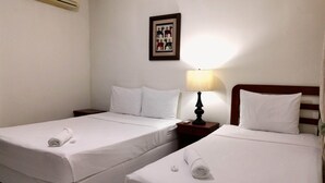 Habitación de hotel con dos camas individuales, ropa de cama blanca, una mesita de noche con lámpara, un cuadro en la pared y un equipo de aire acondicionado.
