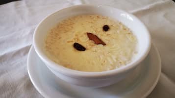 Uma taça de sobremesa cremosa com passas sobre um prato branco, colocada sobre uma toalha de mesa branca.
