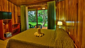 A wooden room with a bed, a TV, a desk, and a window with curtains. - Mar Inn Bed & Breakfast (Monteverde)