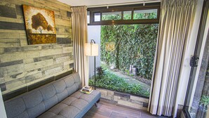A modern room with a grey sofa, a painting on the wall, a lamp, and a view of greenery through a window. - Mar Inn Bed & Breakfast (Monteverde)