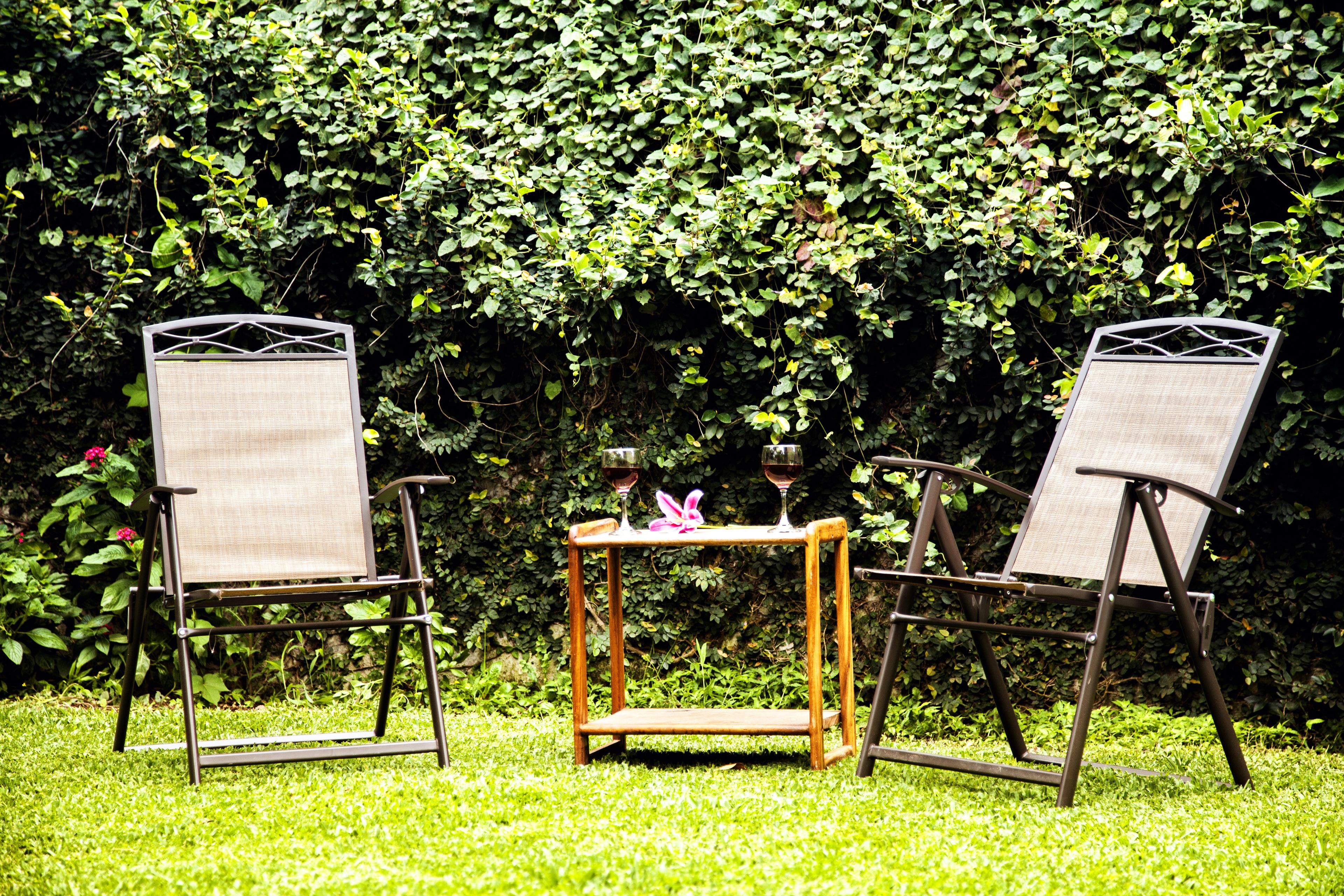 Duas cadeiras e uma pequena mesa com dois copos de vinho em um jardim.