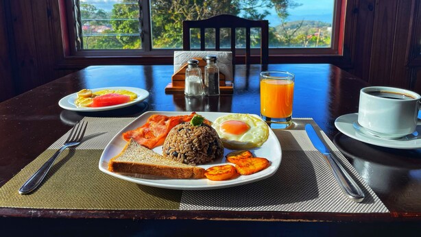 A breakfast table with plates of food, a glass of orange juice, and a cup of coffee. - Mar Inn Bed & Breakfast (Monteverde)
