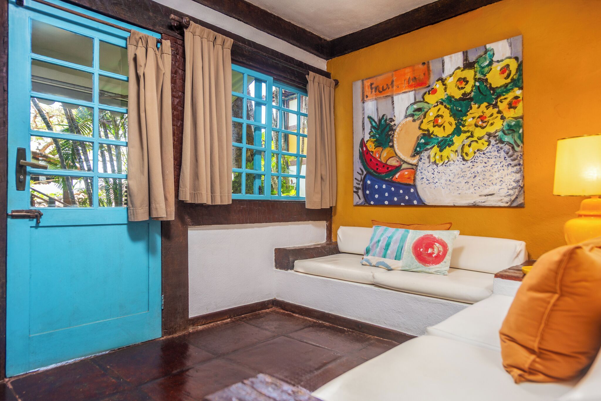 A room with a blue door, a white sofa, a painting of fruit, and a yellow lamp.