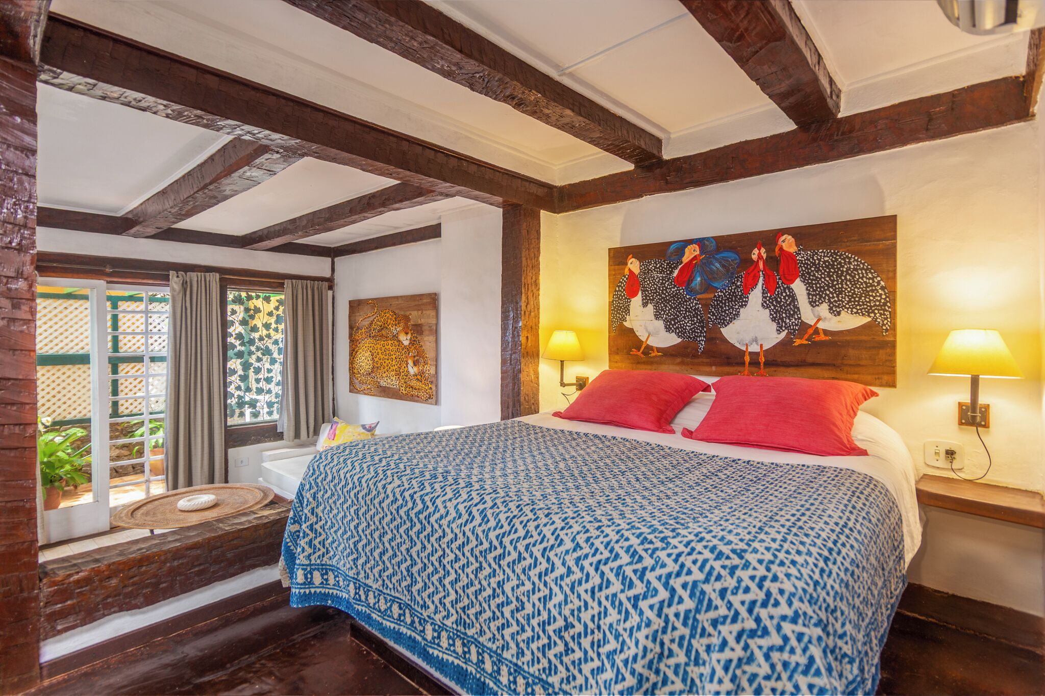 A bedroom with a bed, a painting, a window with curtains, and a lamp.