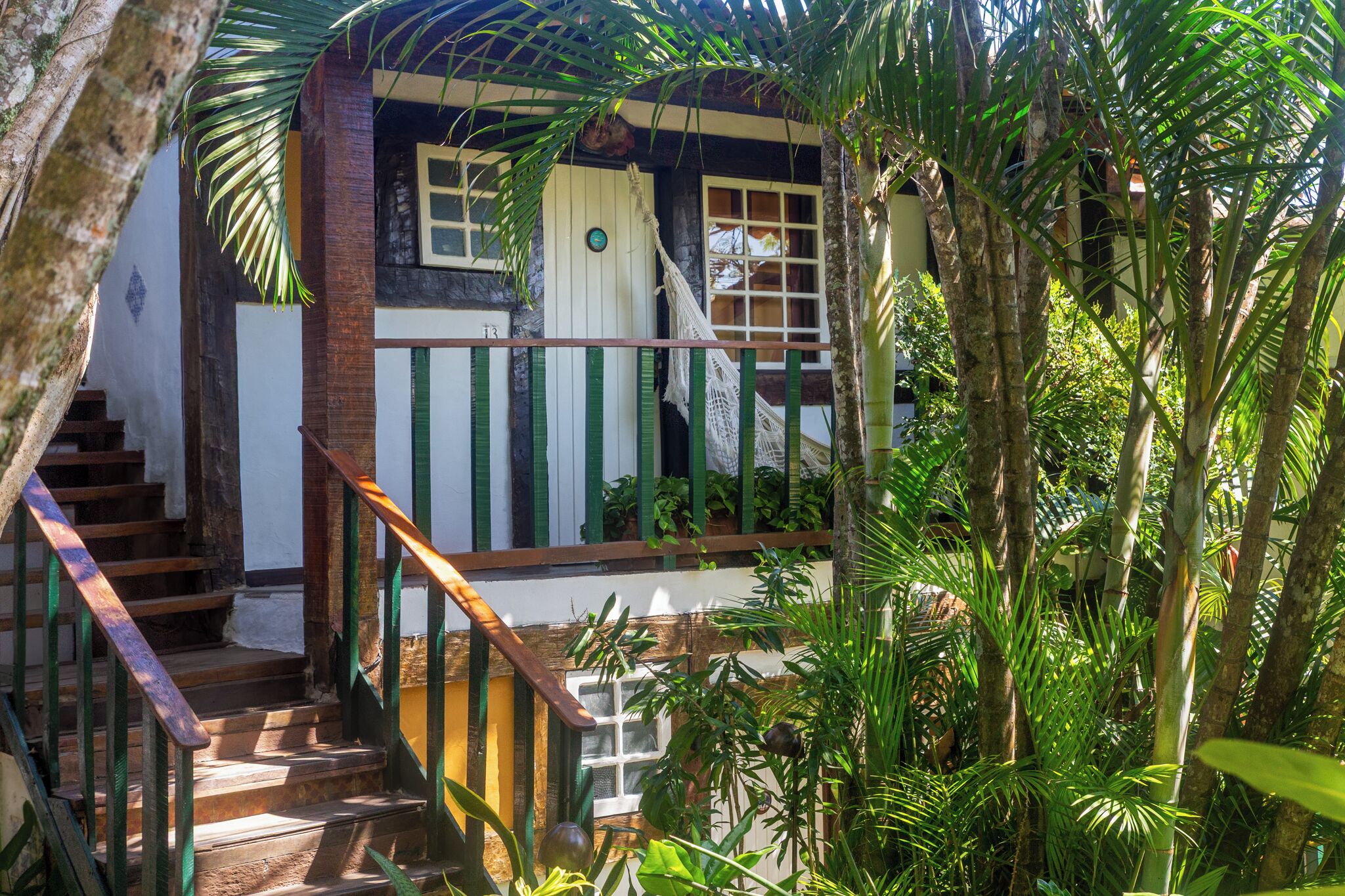 Una casa de madera rústica con escalera, rodeada de abundante vegetación.