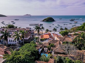 A coastal town with terracotta-roofed buildings, a marina with boats, and a small island in the distance. - Pousada Vila do Mar (Búzios)