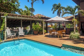 Un espace piscine avec des chaises longues, un coin salon abrité et des palmiers.