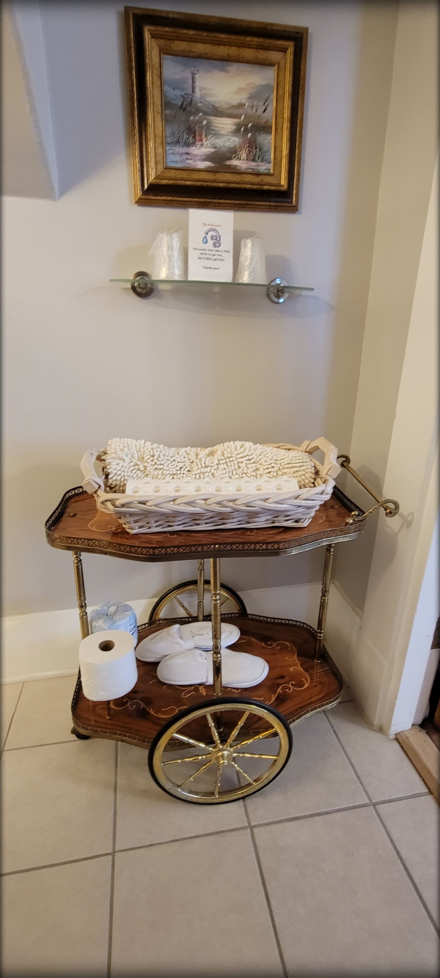 A wooden cart with a white knitted item, a roll of toilet paper, and a pair of white slippers.