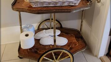 A wooden cart with a white knitted item, a roll of toilet paper, and a pair of white slippers.