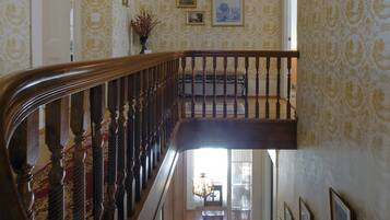 A grand staircase with a wooden handrail and balusters, leading to a landing with a chandelier and framed pictures on the wall.