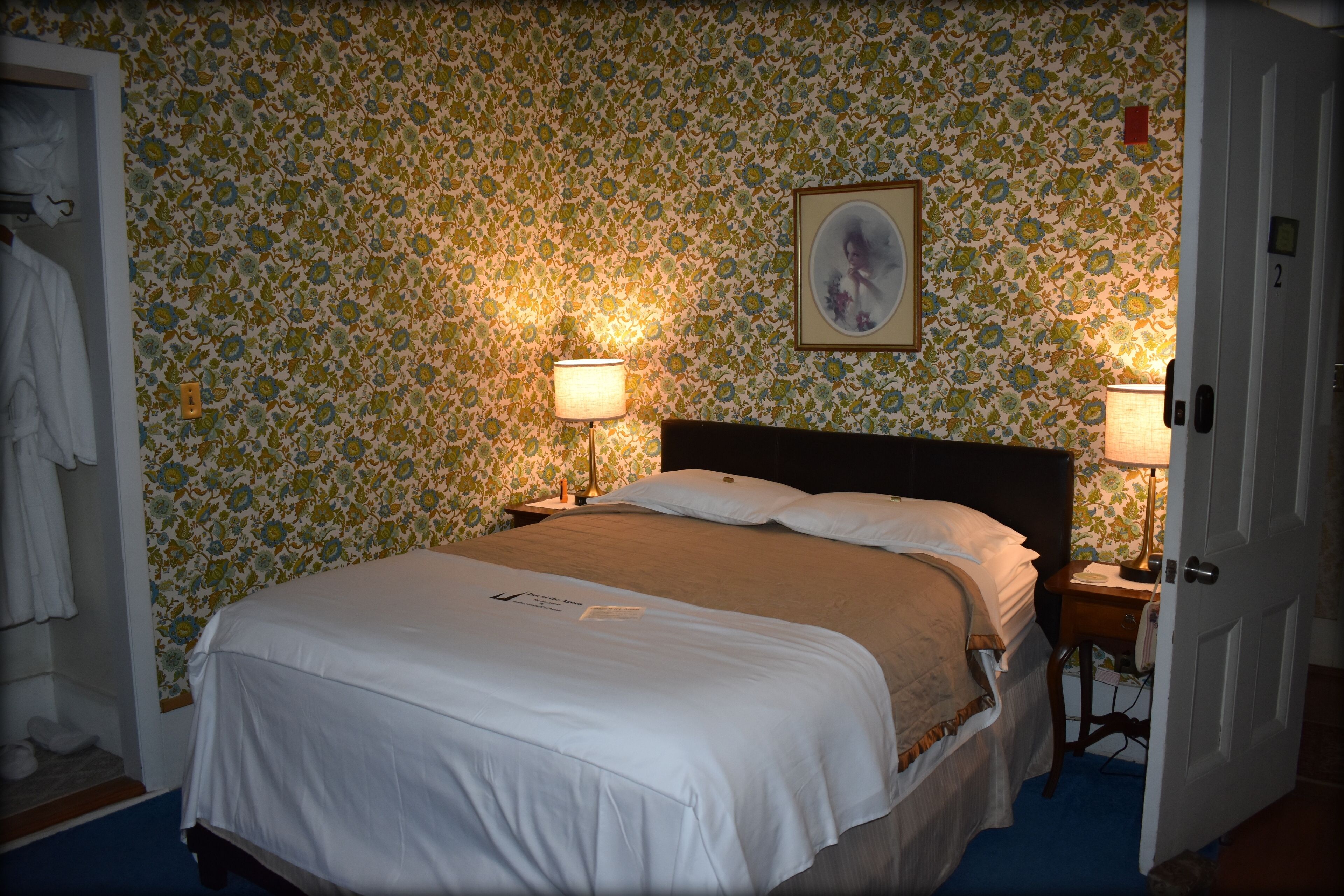 A bedroom with floral wallpaper, a bed with white linens, two bedside lamps, and a door with a number.