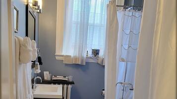 A narrow bathroom with a bathtub, a sink, and a window with sheer curtains.