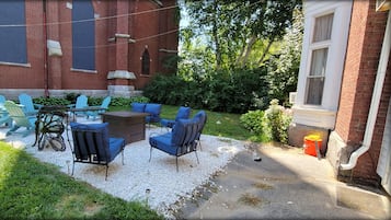A patio area with outdoor seating, a brick building, and a grassy lawn.