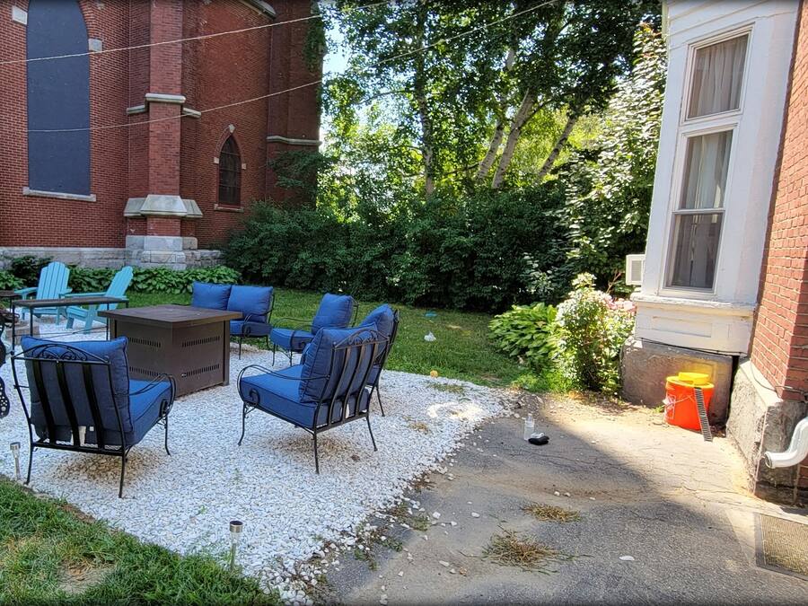 A patio area with outdoor seating, a brick building, and a grassy lawn.