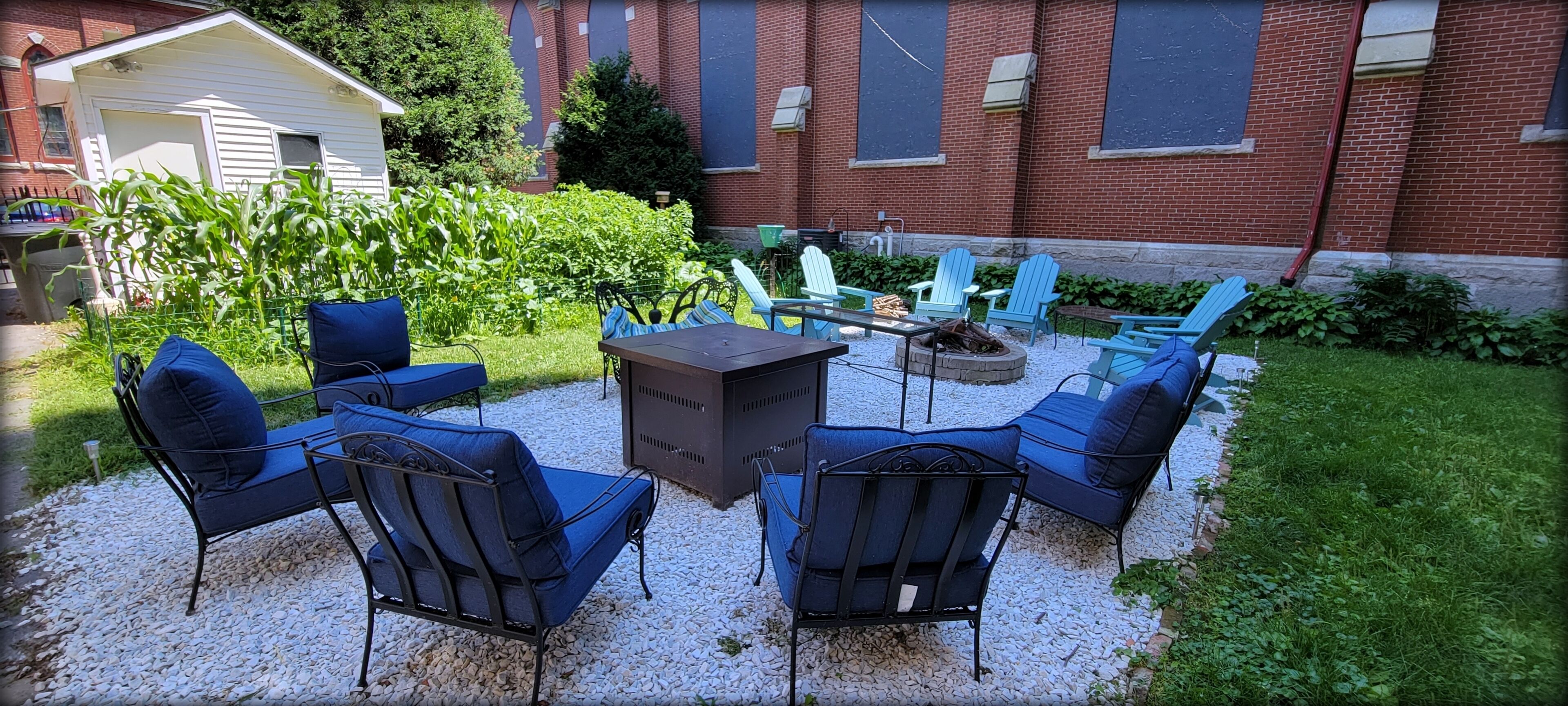 Een terras met buitenmeubilair, een vuurkuil en een bakstenen gebouw op de achtergrond.
