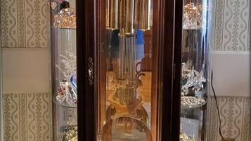 Un reloj de pie con puerta de cristal, mostrando la esfera y el péndulo en su interior.