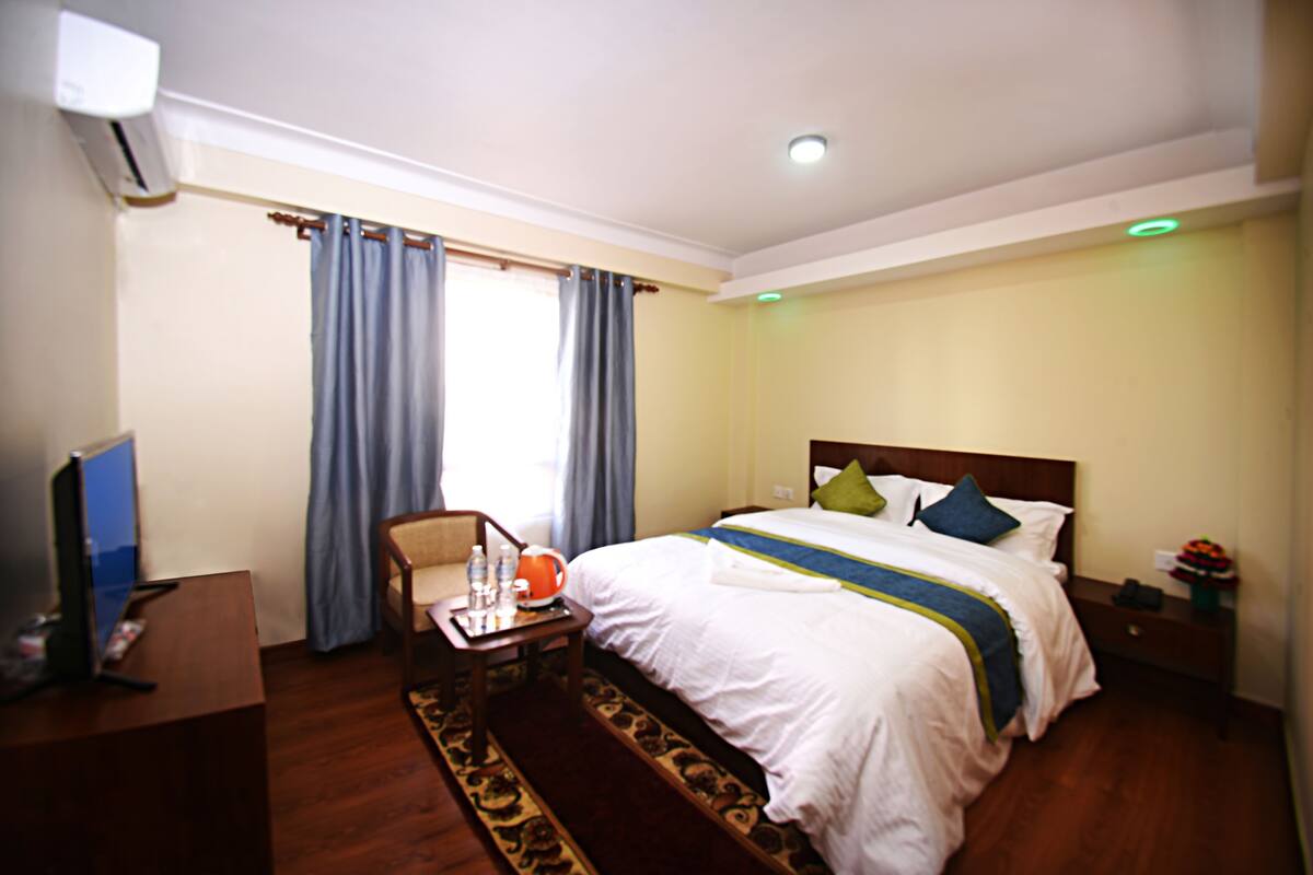 A hotel room with a bed, a desk with a chair, a television, and a window with curtains.