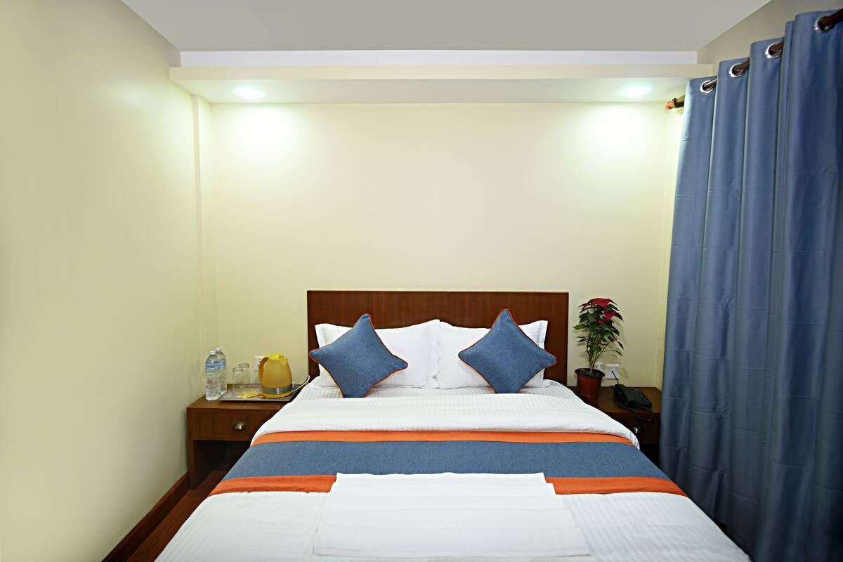 A neatly made bed with a wooden headboard, a bedside table with a lamp, and a potted plant.