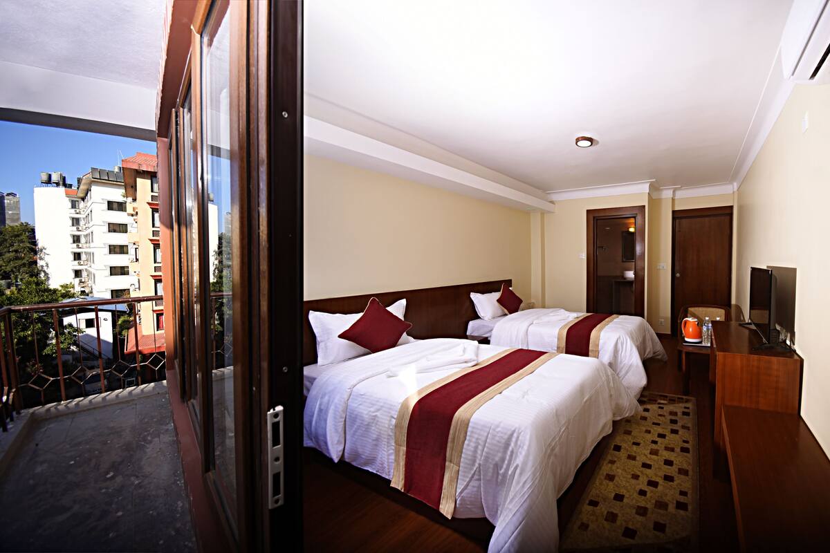 A hotel room with two beds, a balcony, and a city view.