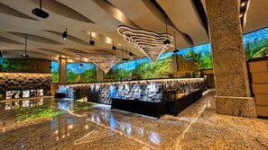 A modern lobby with a long reception desk, a large digital screen displaying a nature scene, and a unique ceiling design. - The Central Park Hotel Songdo (Incheon)