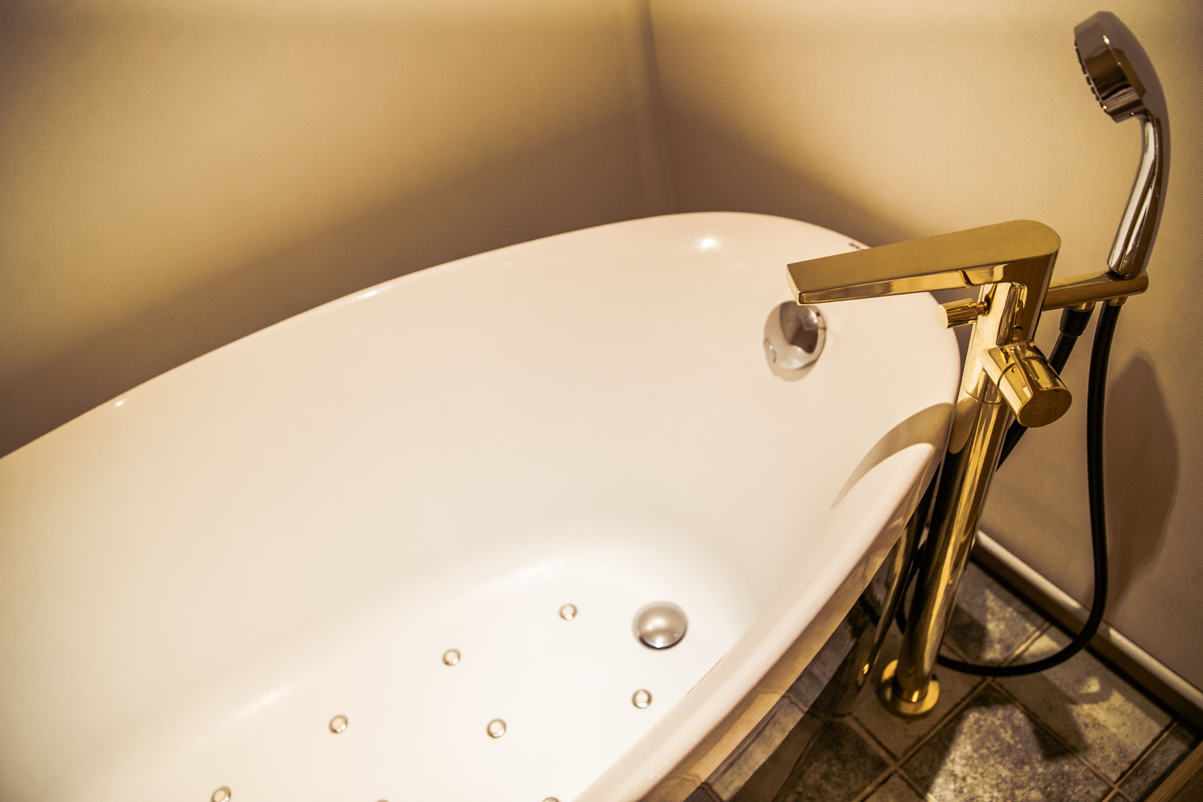 Eine weiße Badewanne mit goldfarbener Armatur und Duschbrause vor einer gefliesten Wand.