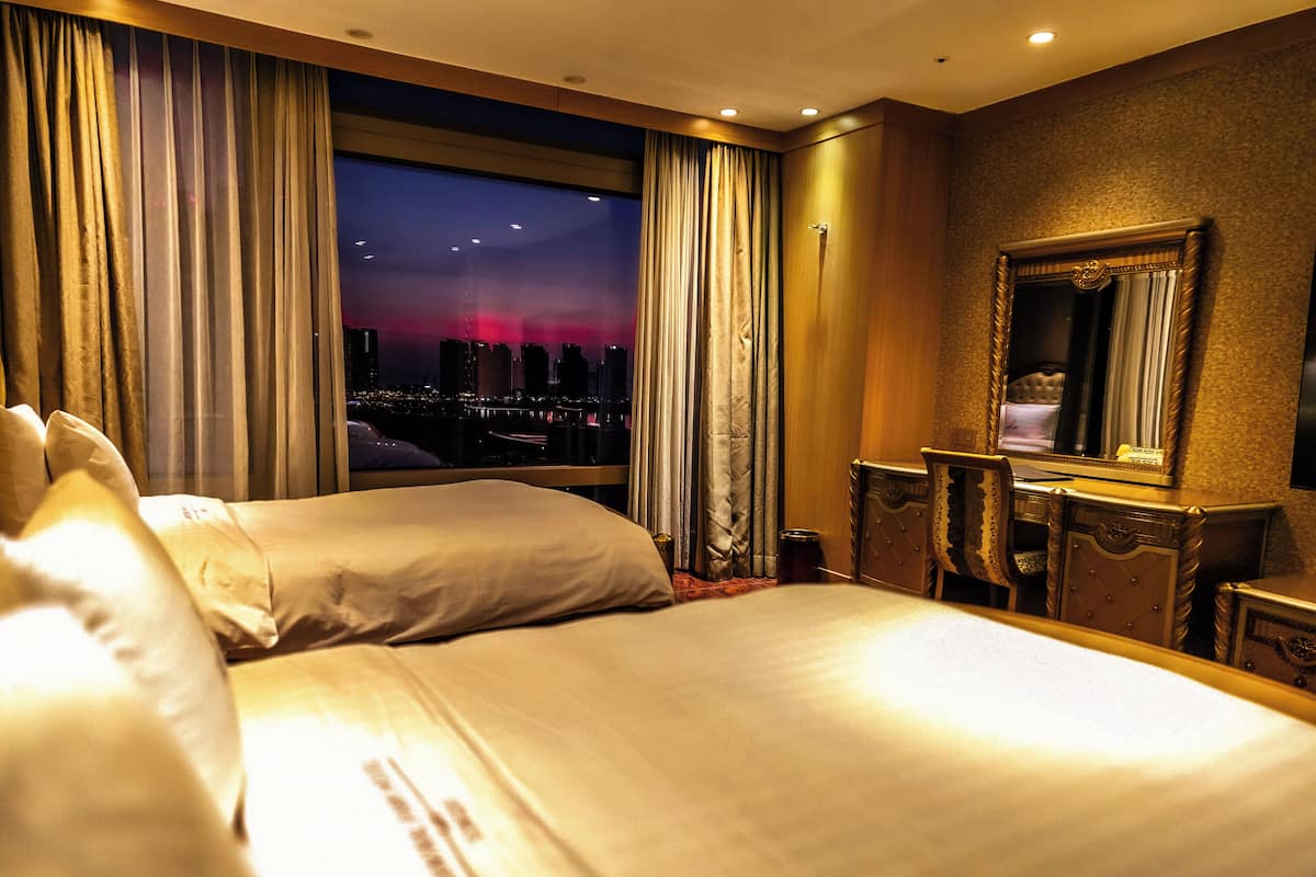 Una habitación de hotel con una cama grande, un escritorio y vistas a un paisaje urbano al anochecer.