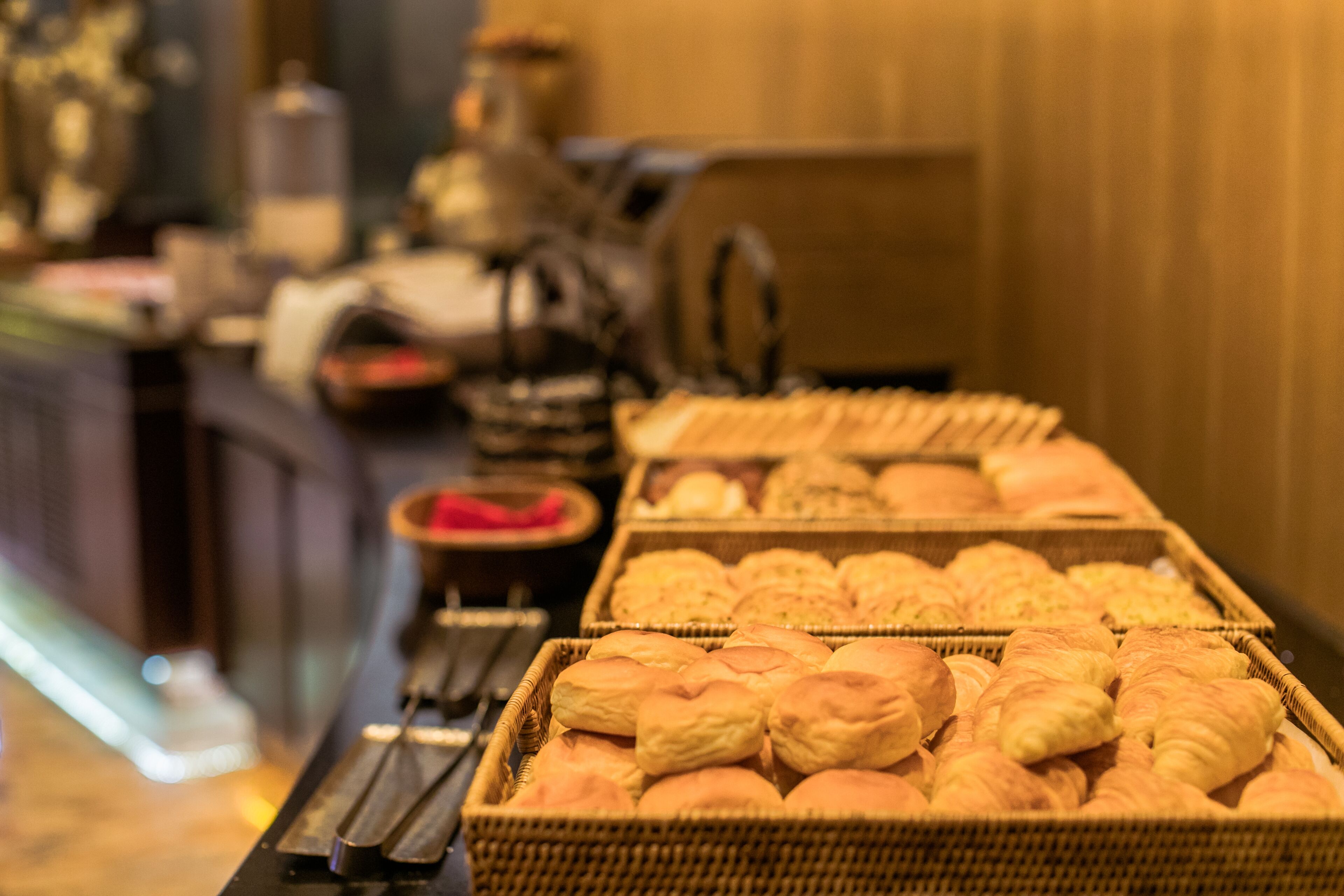Une table de buffet garnie de diverses viennoiseries, notamment du pain et des pâtisseries, présentées dans des paniers en osier.