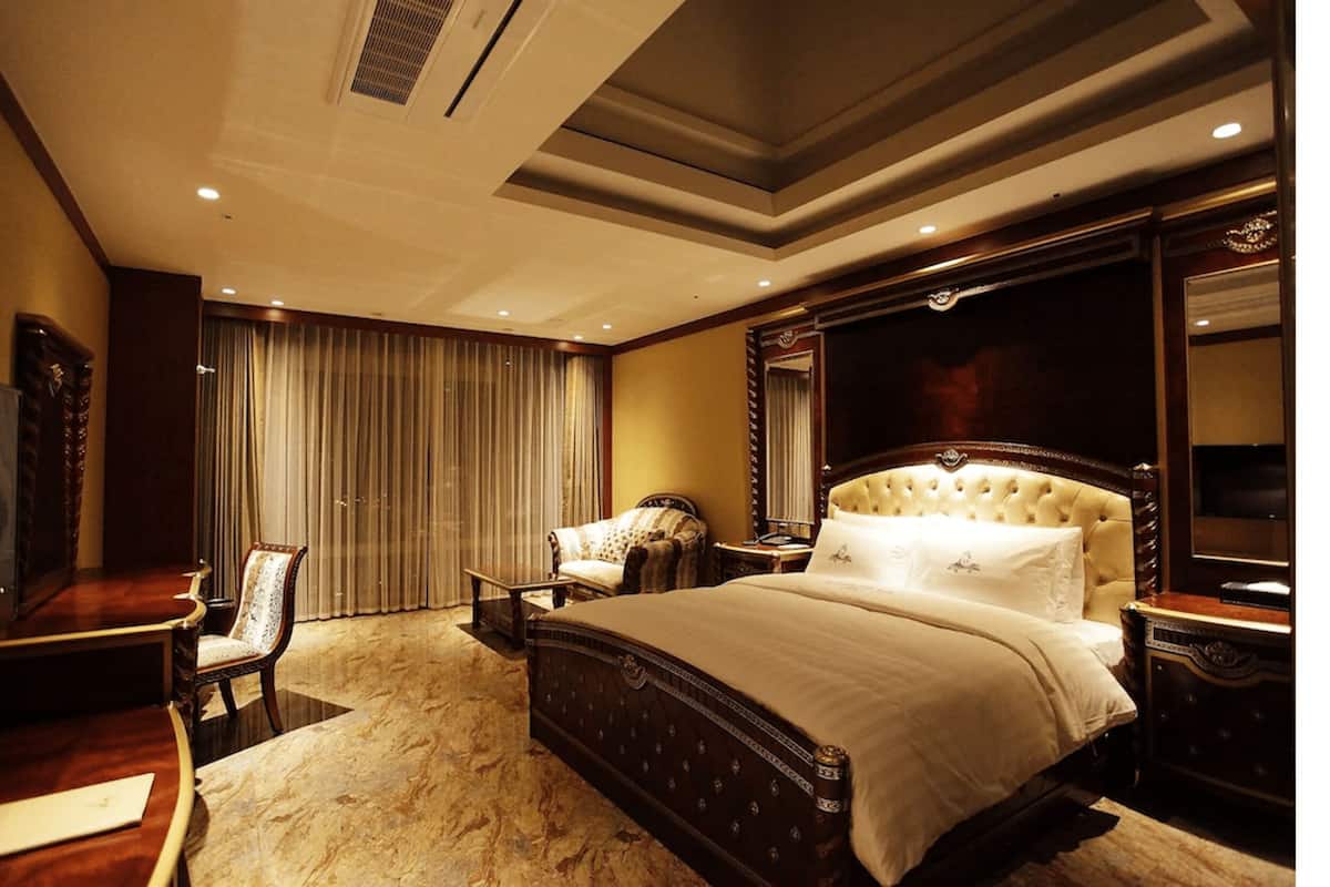 Un dormitorio espacioso con una cama grande, una zona de estar con una silla, un televisor y un espejo.